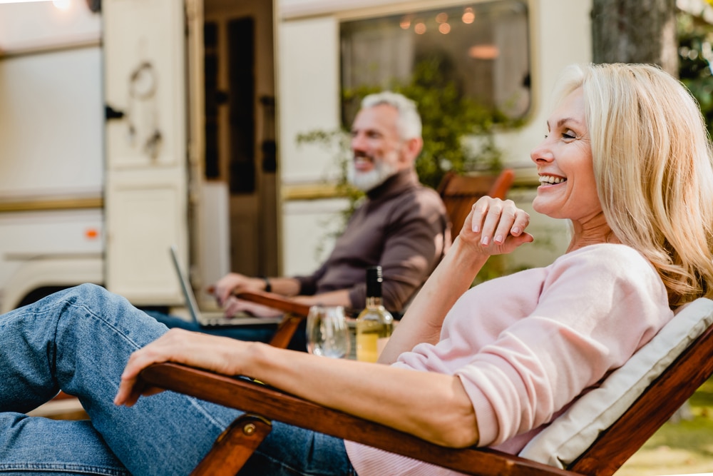 A couple laughing and smiling while enjoying drinks outside of their RV